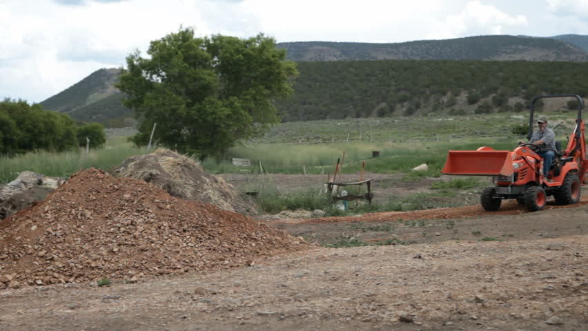 tractor backhoe driving and working on a farm moving dirt. Building 